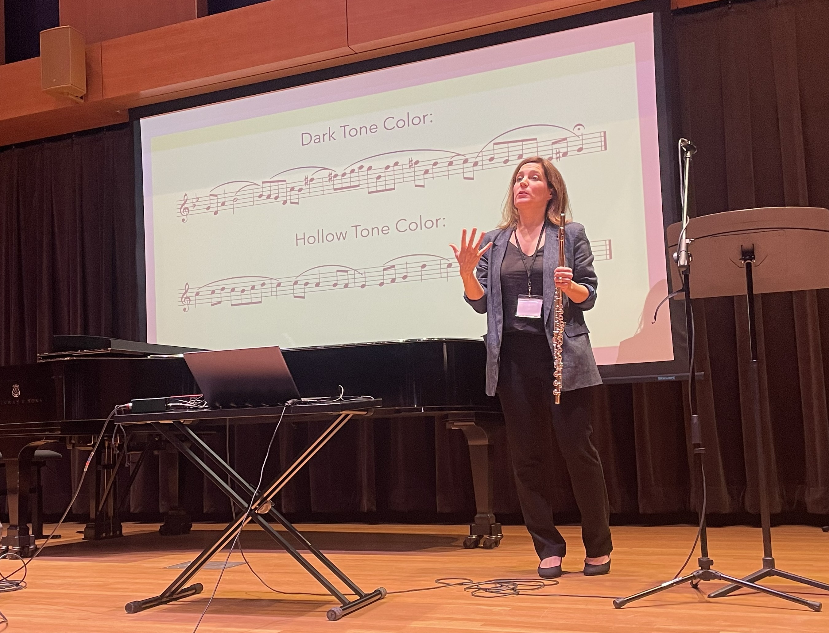 Abigail Walsh presenting a clinic on flute tone color with musical examples projected behind her.